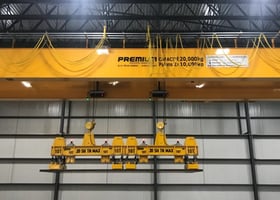 pont roulant jaune équipé d'une aimant soulevant une plaque d'acier