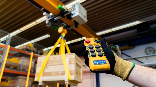 main tenant une telecommande Magnetek-Flex avec un pont roulant en image de fond