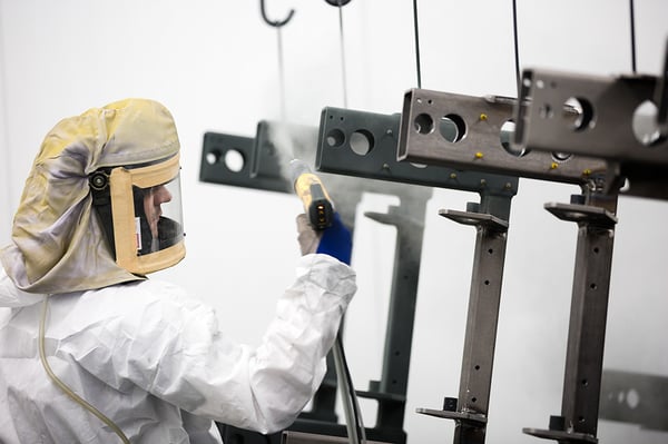 a worker is painting parts suspended from hoists in a paint booth 